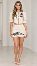 Front view of model wearing ivory floral embroidered tie-front crop top and scalloped mini skirt set