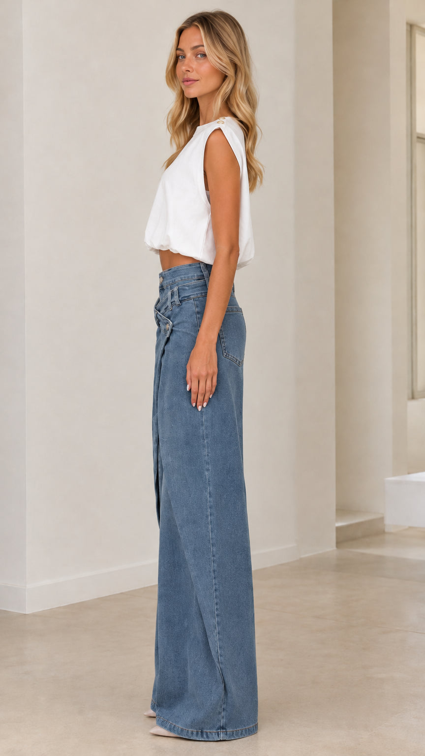 Side profile view of model wearing medium blue asymmetrical wide leg denim pants