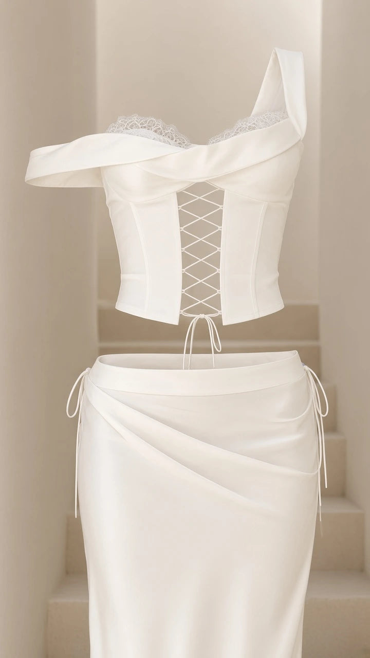 Product flat view showing white lace-up corset top with lace trim and matching draped skirt